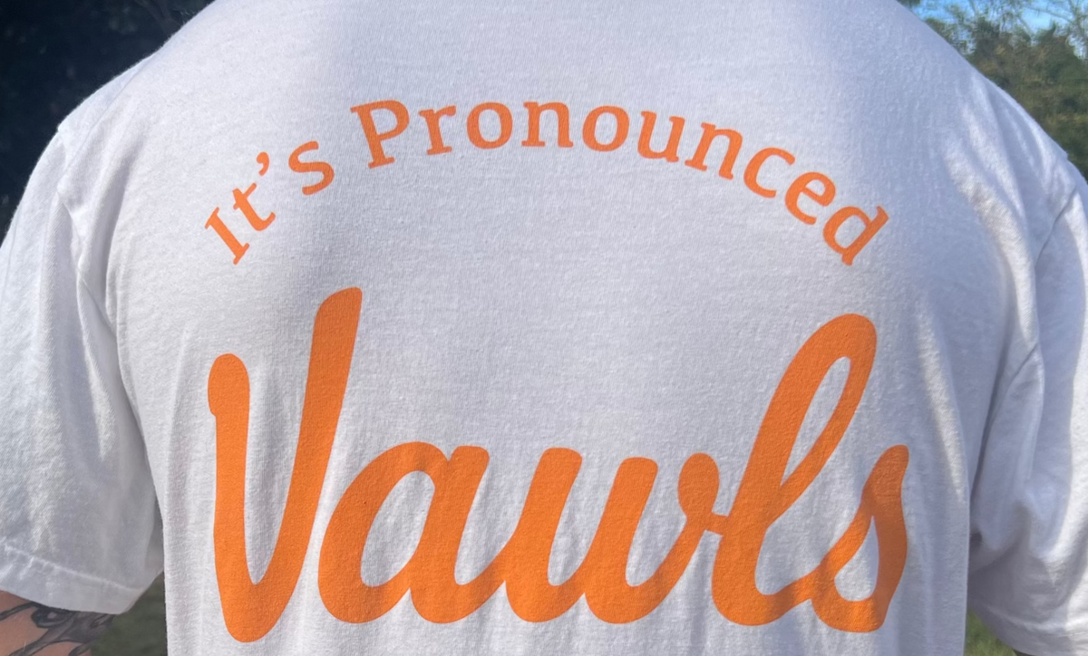 Person wearing a white t-shirt with 'It's Pronounced Vawls' printed on the back outdoors.